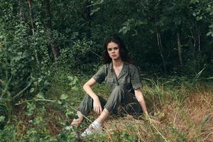 bonito mujer en mono se sienta en seco césped en naturaleza bosque foto