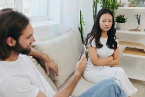 A man looks at the phone screen during an argument with his girlfriend. The angry and hurt woman looks in his direction and is sad. Family discord at home, phone addiction photo