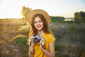 alegre mujer participación un cámara en su manos rojo labios sonrisa en un sombrero al aire libre foto