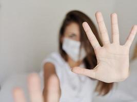 aggressive woman in a medical mask covers the camera with her hands on a light background pandemic coronavirus photo