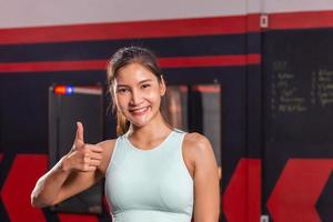 Portrait of Young sports woman smiling and looking at camera, Happy girl showing thumbs up in fitness gym photo