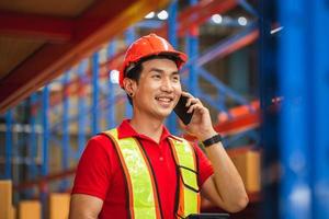 Cheerful warehouse worker with smartphone and digital tablet checking inventory in warehouse, Worker man working in warehouse photo