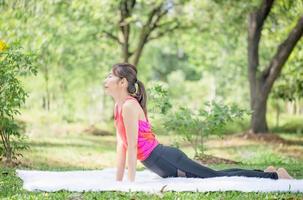 joven mujer haciendo ejercicios en yoga actitud en el parque, lado ver de Delgado deportista haciendo extensión ejercicio a verano verde parques foto