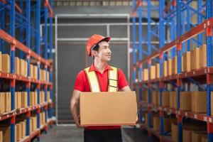 Male worker in hardhat holding cardboard box walking through in retail warehouse, Warehouse worker working in factory warehouse photo