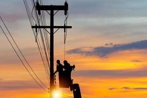 la silueta de un oficial electricista sube a un poste y usa un teleférico para mantener un sistema de línea de alto voltaje, la sombra de un trabajador reparador de liniero electricista en el trabajo de escalada en un poste de energía eléctrica foto