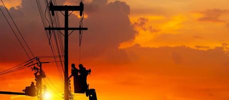 Silhouette of Electrician officer climbs a pole and uses a cable car to maintain a high voltage line system, Shadow of Electrician lineman repairman worker at climbing work on electric post power pole photo