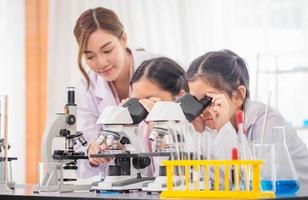 Elementary science class, Child girl looking at slides in through microscope, Science laboratory, Little kids with teacher in school laboratory looking in microscope photo