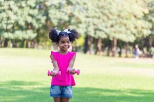 Happy kid girl exercising with dumbbell in park. Active child playing outdoor in the park. photo