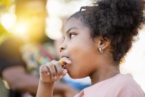 niño niña con anillo popular caramelo en el parque, muchachas disfrutar anillo caramelo estallidos, niños jugar al aire libre foto