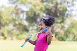Happy kid girl playing with soap bubbles. Active child playing outdoor in the park photo