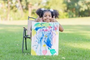 pequeño niño niña muestra su pintura trabajar. linda niño espectáculo pintura trabajo en el jardín foto