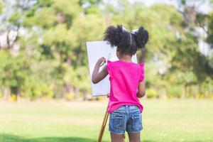 espalda ver de niño niña pintura en lona en el jardín, contento niño niña dibujo un imagen al aire libre foto