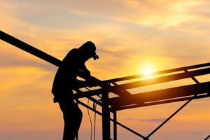 silueta de soldador trabajador en edificio sitio, construcción sitio a puesta de sol en noche hora foto