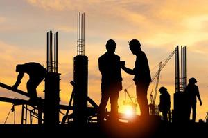 Silhouette of Engineer and worker checking project at building site background, construction site at sunset in evening time photo