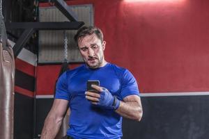 Strong boxer man using smartphone in gym photo