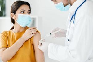 lado ver de médico inyectando vacuna dentro hombro de paciente vistiendo médico máscara en hospital epidemia foto