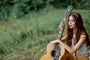 Happy hippie woman with a guitar relaxing in nature sitting on a plaid smiling and enjoying the view. Lifestyle in harmony with nature and self photo