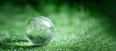 Close up of crystal globe resting on green grass with blur nature background, earth day or world environment day concept. Green world and sustainable conservation of forest resources. photo