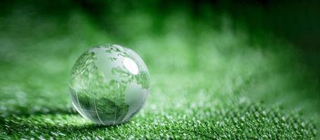 Close up of crystal globe resting on green grass with blur nature background, earth day or world environment day concept. Green world and sustainable conservation of forest resources. photo