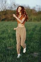 un mujer trabajos fuera y carreras mediante el campo en el parque con un sonrisa en un bueno estado animico mirando a el hermosa verano naturaleza alrededor su foto