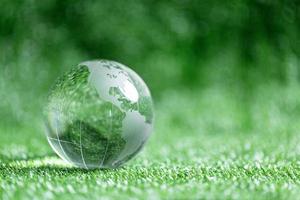 Close up of crystal globe resting on green grass with blur nature background, earth day or world environment day concept. Green world and sustainable conservation of forest resources. photo