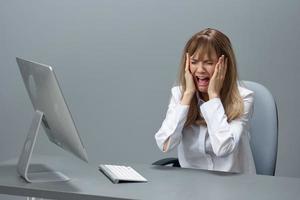 Crying pretty blonde businesswoman made critical mistake using desktop computer touch cheeks sitting in gray modern office. Remote Job, Technology And Career Profession Concept. Copy space photo