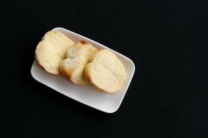 Half round shape bread and fresh butter with sugar in row on rectangle white dish and black background. photo