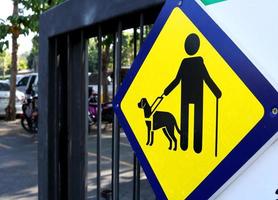 Blind man and dog sign on yellow square shape plate hanging on painted black metal door of pubic park. Beside view. photo