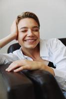 mujer acostado a hogar en el sofá retrato con un corto Corte de pelo en un blanco camisa, sonrisa, depresión en adolescentes, hogar fiesta foto