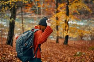 woman in a sweater with a backpack resting in a park near the river in nature in autumn photo
