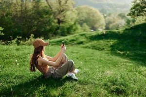 Happy woman blogger lying on the grass in the park and smiling with her phone in her hands against the backdrop of a summer natural landscape with sunlight photo