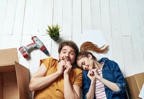 a man and a woman lie on the floor among boxes and a flower in a pot moving photo