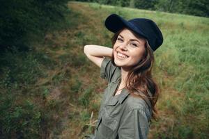 mujer en el bosque alegre sonrisa verde traje negro gorra recortado Mira viaje foto