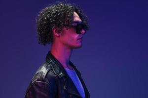 Cyberpunk style curly man leather jacket mirror eyewear looks aside posing isolated on color pink blue studio background. Cool fashion offer. Huge Seasonal Sale New Collection concept. Copy space ad photo