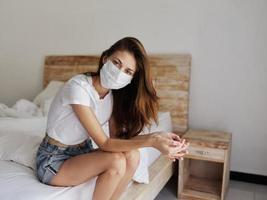 woman wearing a medical mask sitting on a bed in a bright room pandemic vacation photo