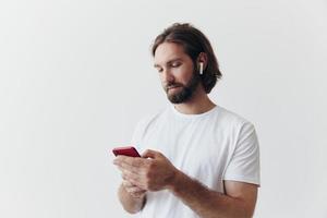 Man blogger holds a phone in his hands and communicates with people online in social networks with a smile and a white t-shirt on a white background photo