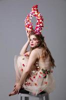 Beautiful girl in a fabulous look with flower horns sits on a chair. Maleficent. Spring or summer beauty. Woman in the image of a flower. photo