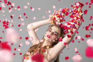 Portrait of a beautiful girl with flower horns in rose petals. Goddess Flora. Beautiful woman with fantastic makeup with flying flowers. Spring girl model. photo