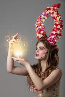 A fabulous girl with floral horns and fantastic make-up holds a glowing ball. Spring or summer beauty. Fantastic woman.Goddess of flowers Flora. photo