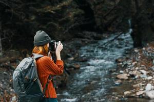 woman with a camera on nature in the mountains near the river and tall trees forest landscape photo