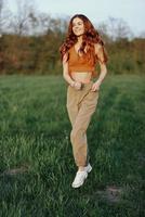 A woman works out and runs through the field in the park with a smile in a good mood looking at the beautiful summer nature around her photo