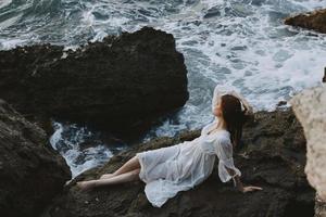 attractive woman with long hair in a white dress lying on a stone in a white dress unaltered photo