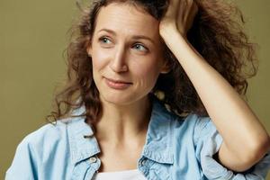 Pensive sad curly beautiful female in jeans casual shirt touch hair looks aside posing isolated on over olive green pastel background. Being Yourself. People Lifestyle emotions concept. Copy space photo