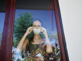 woman in the window wearing a medical mask sad look lockdown photo