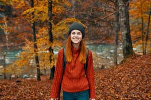 mujer en un sombrero con un mochila y un suéter es descansando en el otoño bosque cerca el río en naturaleza foto