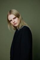 Blonde looks over her shoulder in a black jacket posing half-turned in the studio on a green background. The concept of stylish fashion photography photo