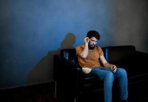 Lonely man in the evening on the couch in front of the TV and popcorn in a plate photo