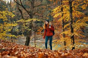 mujer turista camina mediante el parque en otoño con un mochila en su espalda y alto arboles paisaje río lago foto