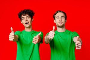 alegre amigos en verde camisetas gesticulando con manos emociones rojo antecedentes foto