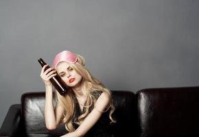 woman with bottle of beer on sofa alcohol addiction sleep mask on head photo